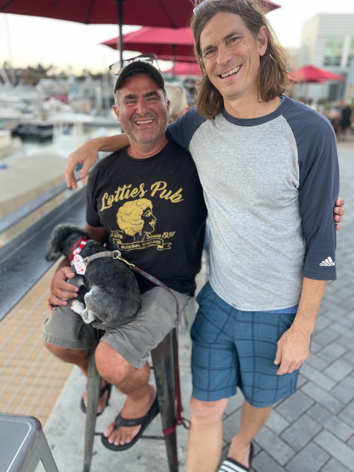Alan at a marina full of boats, with a small dog and a friend